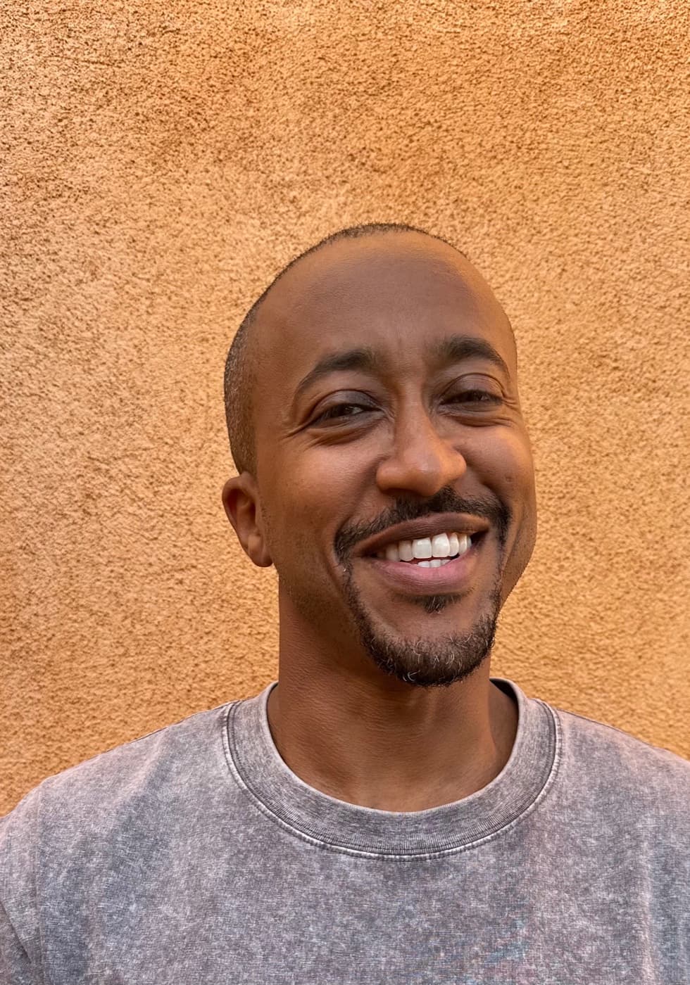 Lull Mengesha, smiling, against an orange stucco wall.