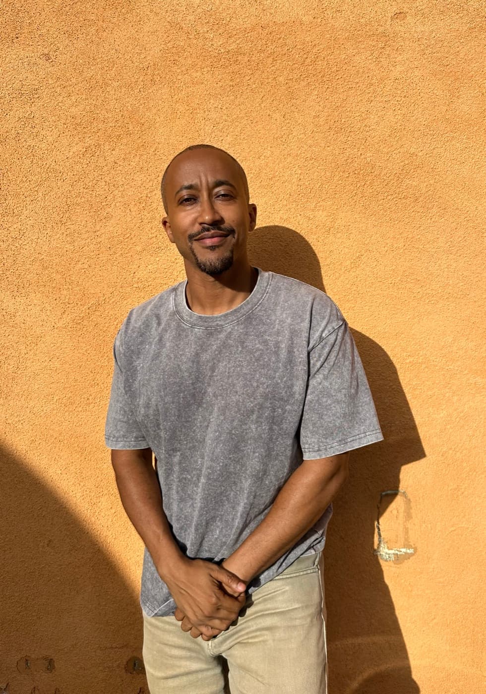 Lull Mengesha, standing against an orange stucco wall.